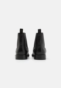 Bottines en cuir noir avec panneaux latéraux élastiques et languettes pour faciliter l'enfilage. Texture lisse et forme arrondie de l'orteil. Semelles en caoutchouc plates.