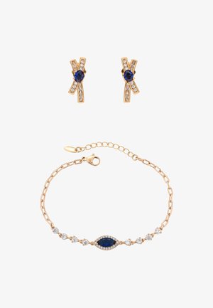 Arany tónusú ékszerszett, amely kereszt alakú fülbevalókat tartalmaz kék és tiszta kövekkel, valamint egy karkötőt marquise csiszolású zafírral és tiszta díszítésekkel.