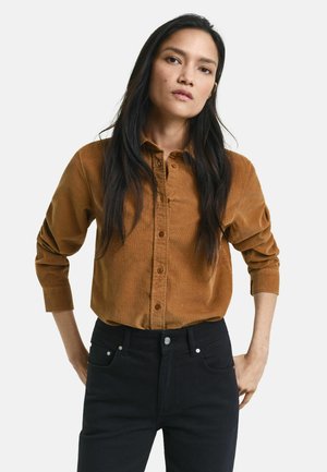 Braune Corduroy-Hemdjacke mit langen Ärmeln, mit Kragen und subtiler Textur, kombiniert mit dunklen Jeans.
