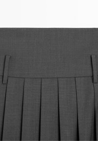 Ceinture d'une jupe plissée gris foncé avec passants pour ceinture, montrant la texture du tissu et des plis réguliers et nets sous la ceinture.