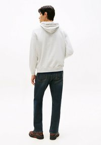 Haut de sweat à capuche gris clair avec cordon de serrage, poignets et ourlet côtelés. Porté avec un jean en denim bleu foncé et des baskets noires avec des accents orange.