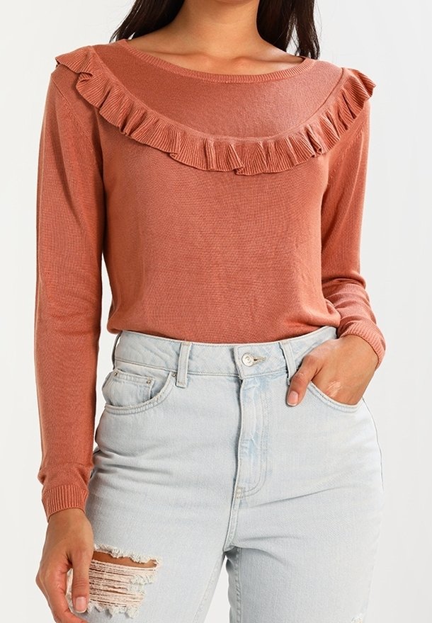 Haut à manches longues couleur rouille avec un col rond orné d'un volant. Assorti à un jean taille haute bleu clair déchiré.