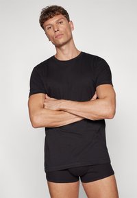 Svart kortermet t-skjorte med crew neck. Stoffet virker glatt og lett, kombinert med svarte tettsittende shorts.