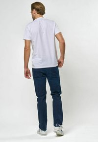 Balta kokvilnas T-krekls, saskaņots ar tumši zilām džinsa biksēm ar taisnu kāju griezumu. Apģērbu papildina balti apavi un gaiss, vienkrāsains fons.