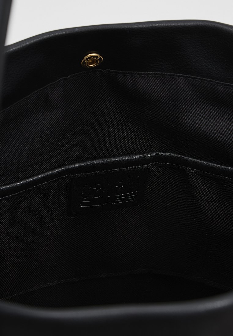 Innenraum einer schwarzen Lederhandtasche mit glatter Textur, goldfarbenem Druckknopfverschluss und einem Etikett, das auf die Innentasche genäht ist. Einfaches Design.