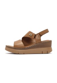 Sandalias de cuña de cuero marrón con una tira ancha, parte trasera ajustable y acento metálico con logo. Suela texturizada proporciona agarre y estabilidad.