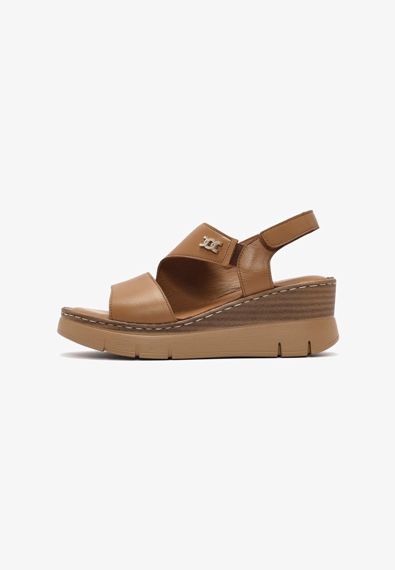 Tan leather wedge sandals with a wide strap, adjustable back, and metallic logo accent. Textured sole provides grip and stability.