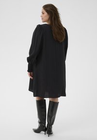 Sort kjole med lange, puffede ærmer og en løs, flydende design. Bæres med knæhøje sorte støvler, som fremhæver tekstur og lagdeling.