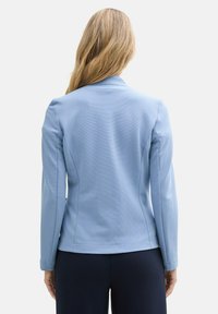 Blazer bleu clair en tissu texturé, coupe ajustée, manches longues et revers crantés, vu de dos.
