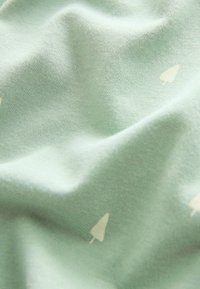 Mjuk grön tyg med små, ljusa trädikoner spridda över ytan och mjuka veck som skapar textur.