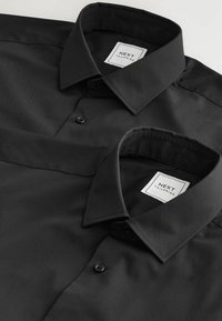 Chemise ajustée noire au toucher doux, présentant un col pointu, une fermeture à boutons et une étiquette indiquant "NEXT TAILORING."