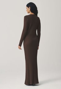 Robe longue marron ajustée en maille côtelée avec manches longues et encolure ronde, présentant une texture lisse et un design longueur totale.