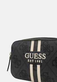 Borsa a zip nera con motivo a logo in rilievo, caratterizzata da strisce bianche e testo "GUESS EST 1981" sul fronte. Materiale sintetico testurizzato.