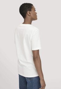 Witte katoenen T-shirt met korte mouwen, eenvoudige stijl, ronde halslijn, gladde textuur, gecombineerd met blauwe denim shorts.