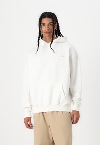 Sudadera blanca con un bolsillo frontal y capucha con cordón. Presenta puños y dobladillo acanalados, fabricada en una tela suave, con un sutil logotipo en el pecho.