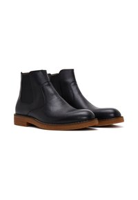 Bottines Chelsea en cuir noir avec finition texturée, panneaux latéraux élastiques et semelles en bois brun. Dotées d'un bout arrondi et d'une couture minimale.