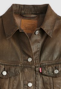 Brun denimjakke med klassisk krage, sølvknapper og skinnmerke. Har to framlommer og en teksturert finish.