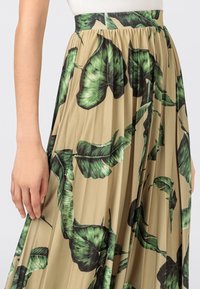 Plisserad kjol med en beige bakgrund och stora gröna och svarta bladmönster. Tyget har en smooth yta som förstärker designen.