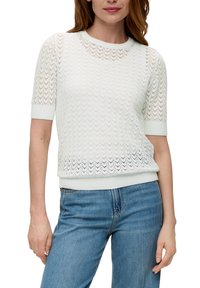 Jasnozielony sweter robiony na drutach z zygzakowatym wzorem, krótki rękaw i ściągacz na dole, zestawiony z jasnoniebieskimi dżinsami.