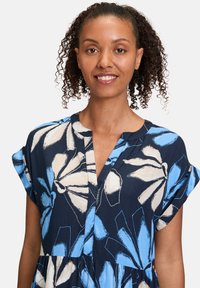 Robe marine avec un motif floral en bleu et crème, dotée d'un décolleté en V, de manches courtes et d'un tissu texturé. Des coutures plates soulignent le design.