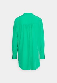 Blouse vert vif à manches longues avec empiècement dos froncé et poignets boutonnés, vue de dos sur fond blanc uni.