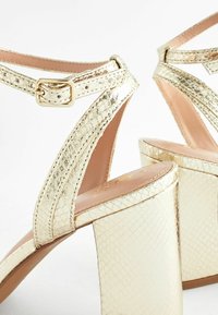 Guld fusk-läder sandaler har en chunky klack, snördesign, justerbar ankelspänne och en texturerad orm-skinmönster.