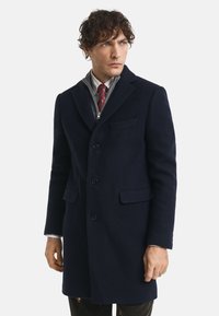 Cappotto di lana navy con un design sartoriale, fronte monopetto e revers a cannello. Presenta due tasche laterali e una vestibilità slim.