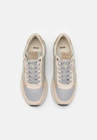 Grauer und beiger Sneaker mit einem Mesh- und Wildleder-Design, ausgestattet mit abgerundeter Spitze, flachen Schnürsenkeln und einem Logo auf der Zunge. Mit strukturierten Akzenten versehen.