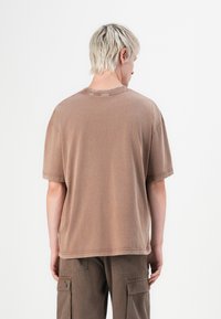 Brun oversized t-skjorte laget av myk bomull med rund hals og korte ermer, med subtile sømdetaljer.
