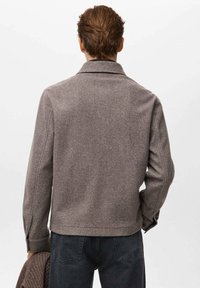 Chaqueta gris de mezcla de lana con cuello de solapa, mangas largas y un ajuste ligeramente estructurado, que presenta detalles de costura sutiles.