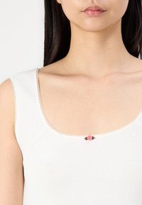 Top blanco sin mangas con un diseño texturizado, escote redondeado y un pequeño acento de rosa rosa en el centro, complementado con un delicado borde de encaje.
