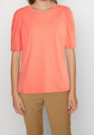 Korallenrosa Kurzarm-T-Shirt mit gepufften Schultern, rundem Ausschnitt und glatter Textur. Kombiniert mit beigen Hosen.