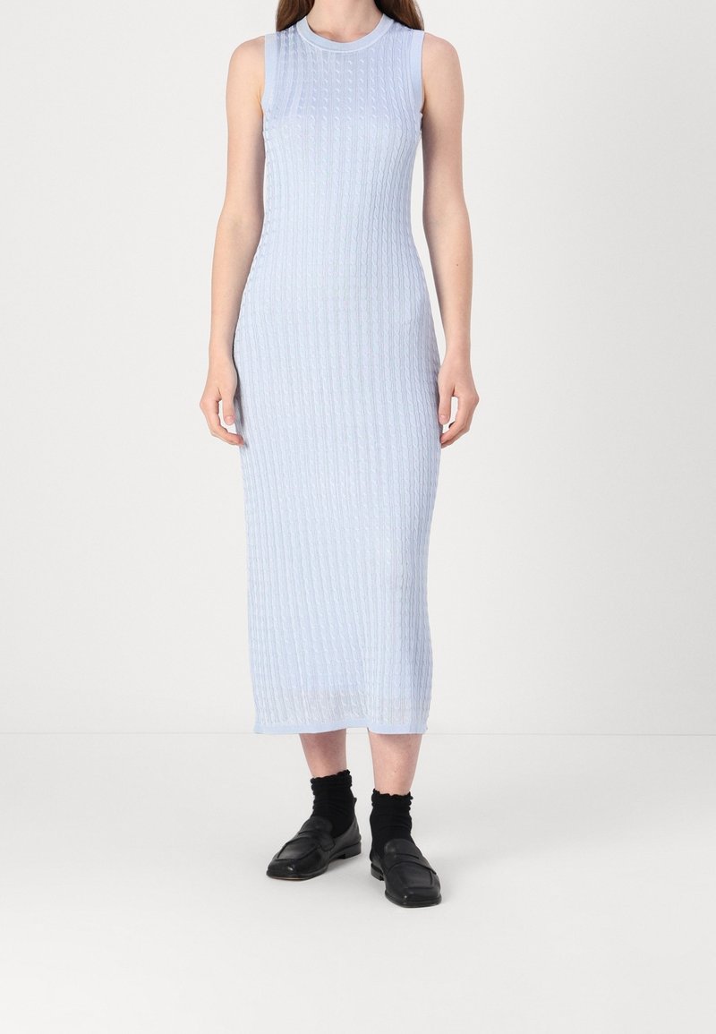 Robe midi bleu clair sans manches avec motif en tricot torsadé, portée avec des chaussettes noires et des chaussures noires à enfiler.