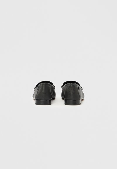Mustad nahast loafers, millel on tekstuuriga viimistlus, madal konts ja ümar nina. Tagantvaade näitab siledad servad ja minimaalsed kaunistused.