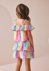Färgglad, lagerpålagd klänning med volanger i ljusblått, rosa och gult mönster. Har axelband och en figurnära överdel, mjuk textur.