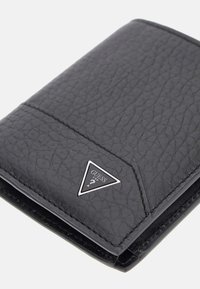 Portefeuille en cuir noir texturé avec un logo en argent en forme de triangle. Présente un design simple et des coutures le long des bords, avec une forme compacte et rectangulaire.