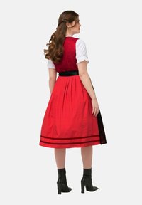 Robe rouge à pois avec un corsage ajusté, une ceinture noire et une jupe plissée. Présente un overlay en dentelle noire au niveau de l'ourlet et une blouse blanche en dessous.