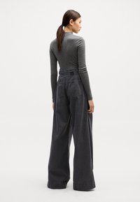 Parte posterior de una camiseta gris de manga larga y pantalones grises de pierna ancha. La camiseta tiene un diseño ajustado; los pantalones presentan una cintura alta, grandes bolsillos y un corte holgado.