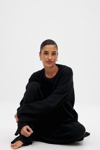 Juodas namų aprangos komplektas pagamintas iš minkštos medžiagos. Viršus turi apvalų iškirpimą ir laisvą siluetą, o kelnes puošia plačios kojos ir atsipalaidavęs stilius.