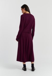 Completo in maglia a due pezzi di un intenso viola scuro, con un top aderente a maniche lunghe e una gonna fluida lunga fino alla caviglia con una leggera texture.