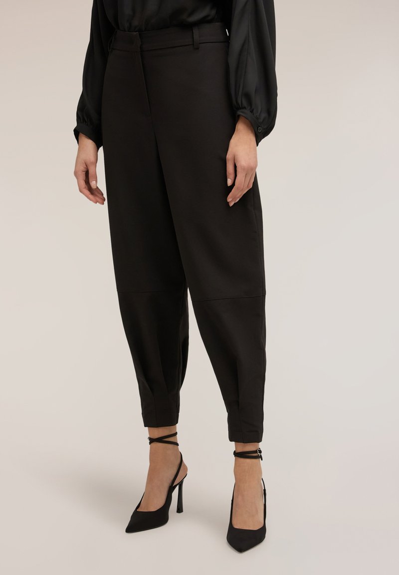 Pantalones negros a medida con cintura alta, piernas entalladas y textura suave, combinados con tacones altos negros de tiras.