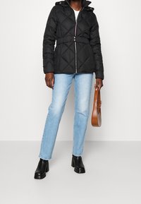 Sort quiltet jakke med hætte, med indsnævret talje, frontlynlås og trykknapper, parret med lyseblå lige bukser og sorte støvler.