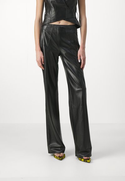 Fekete bőrnadrágok szabott fazonnal, varrással és sima textúrával rendelkeznek. Sárga díszítésű, hegyes orrú magassarkúval viselve.