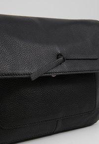Schwarze Leder-Clutch mit strukturiertem Oberflächen, einem Umschlagdeckel und einem einfachen Verschluss mit einem schlanken Tragegurt.