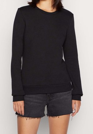 Woman wearing a plain black long-sleeve crewneck sweatshirt and black denim cutoff shorts with frayed hems.