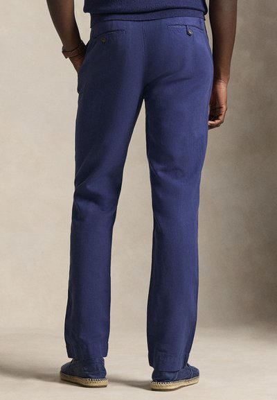 Marineblauwe linnenbroek met een rechte pasvorm, voorzien van twee achterzakken en knoopdetails. De textuur oogt glad en licht.