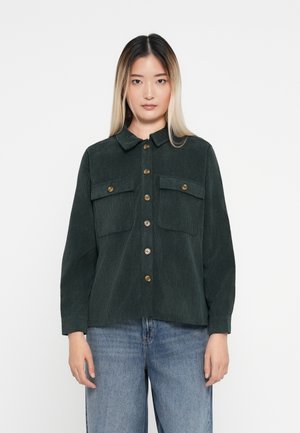 Veste en velours côtelé vert foncé avec col, deux poches poitrine et boutons dorés. Manches longues avec poignets à bouton.