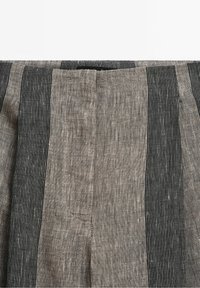 Gros plan d'un pantalon en tissu de lin avec de larges rayures verticales noires et grises avec de fines lignes blanches en pointillés.