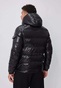 Doudoune noire à texture brillante et matelassée ; dotée d'une capuche, de poches latérales et de poignets élastiques ; taille cintrée pour une silhouette ajustée.