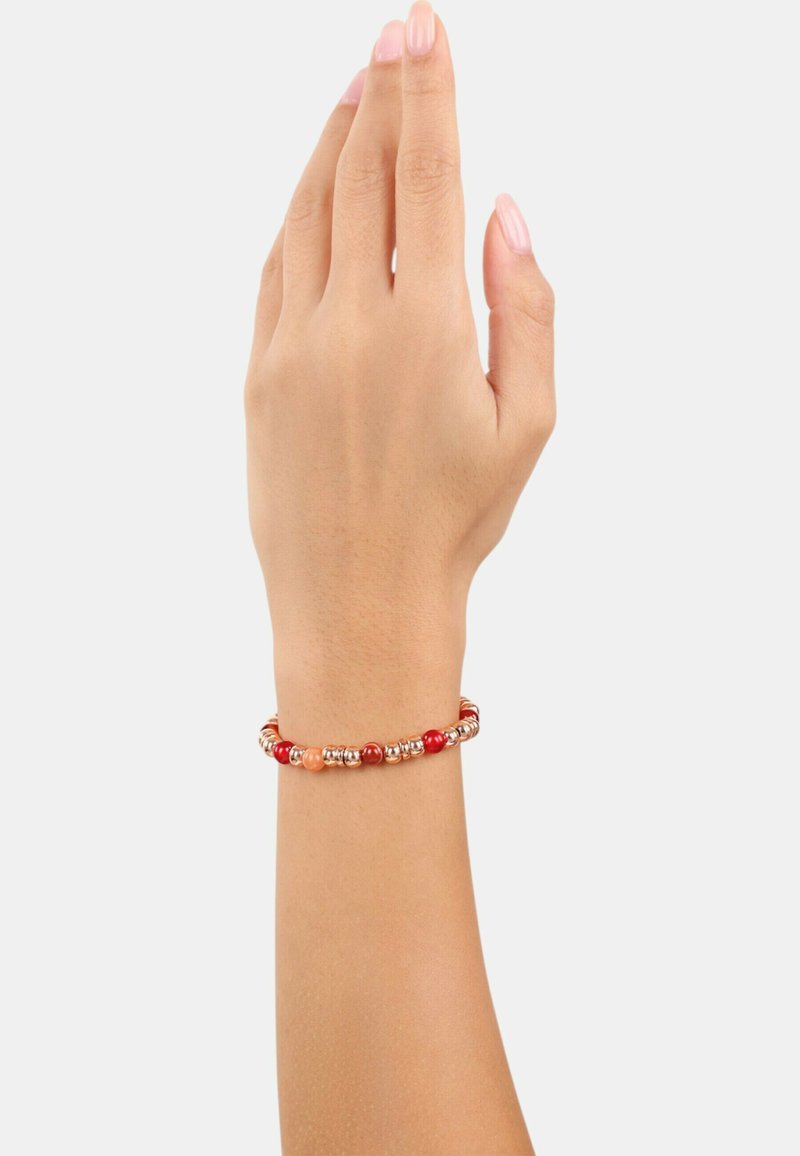 Pulsera de cuentas rojas con acentos metálicos, que presenta tonos variados de cuentas rojas y naranjas, mostrada sobre una mano humana contra un fondo neutro.